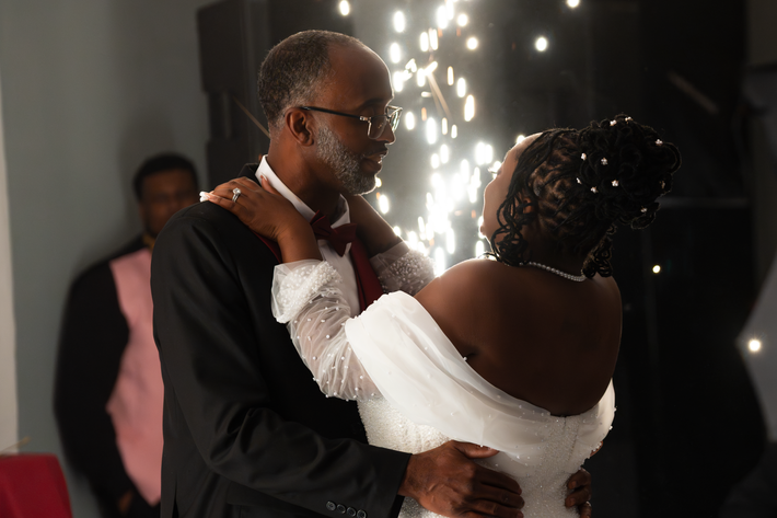 Man and woman dancing closely in a festive setting with lights in the background